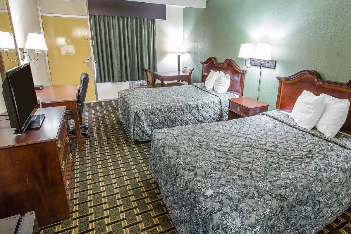 A hotel room with two beds, a desk with a computer, a chair, and a small table.