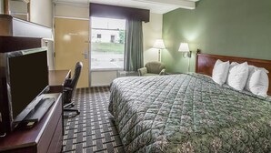 A hotel room with a bed, a desk with a computer, a chair, a lamp, and a view of the outdoors through a window. - Rodeway Inn Laurens (Laurens)
