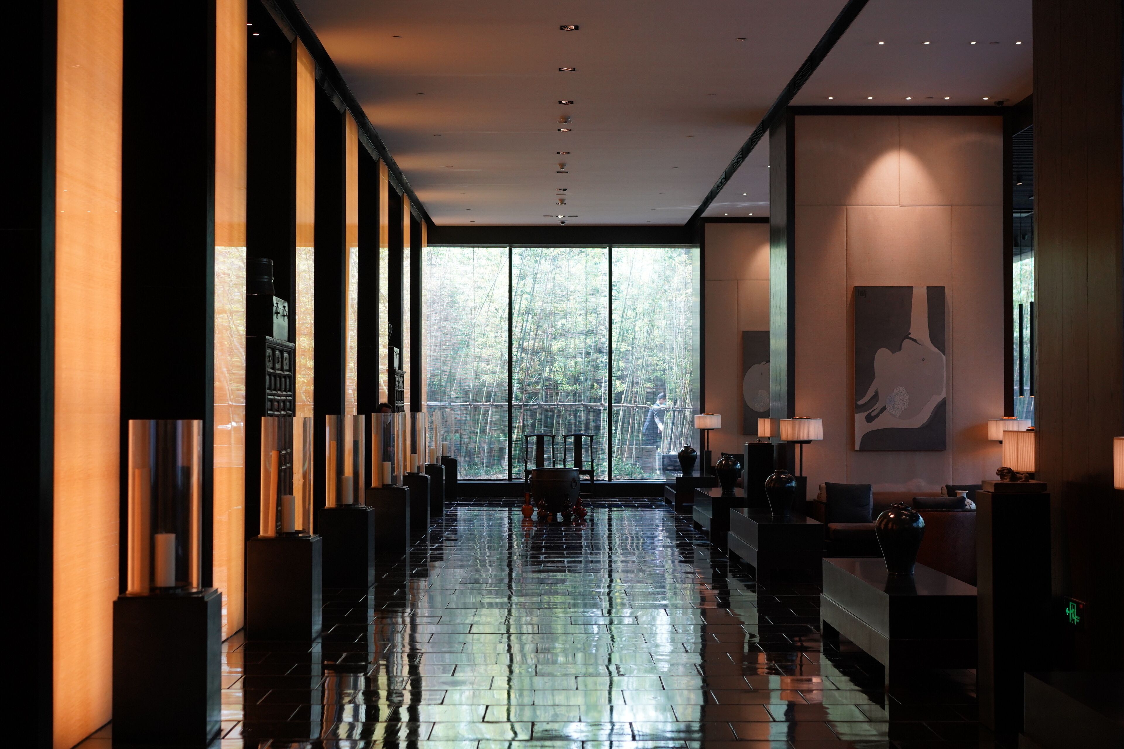 A modern hotel lobby with a reflective floor, large windows, and a reception desk.