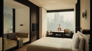 Une chambre d’hôtel moderne dotée d’un grand lit, d’un canapé, d’une table à manger et offrant une vue sur la ville grâce à de grandes fenêtres.
