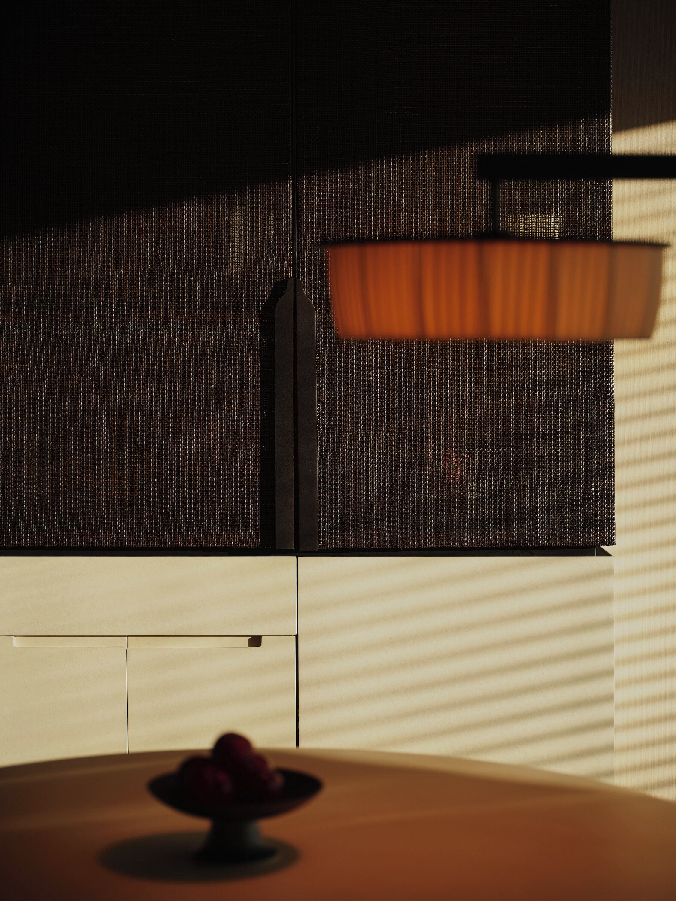 A modern interior with a dark textured wall, a wooden table with a bowl of fruit, and a window with blinds.