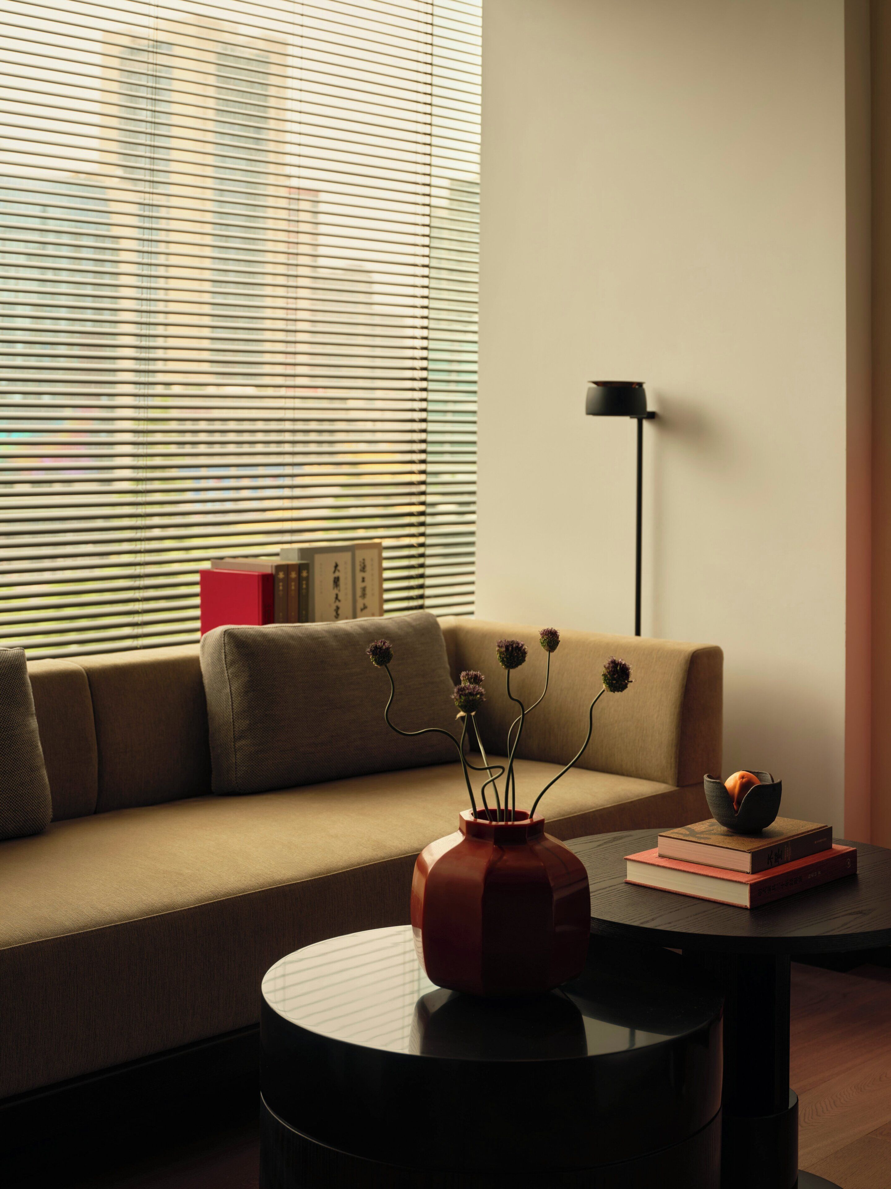 A modern living room with a sofa, a round coffee table, a vase with flowers, and a floor lamp.