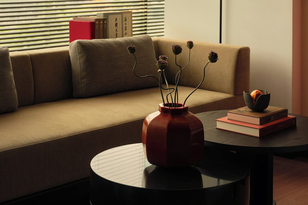 A modern living room with a sofa, a round coffee table, a vase with flowers, and a floor lamp.