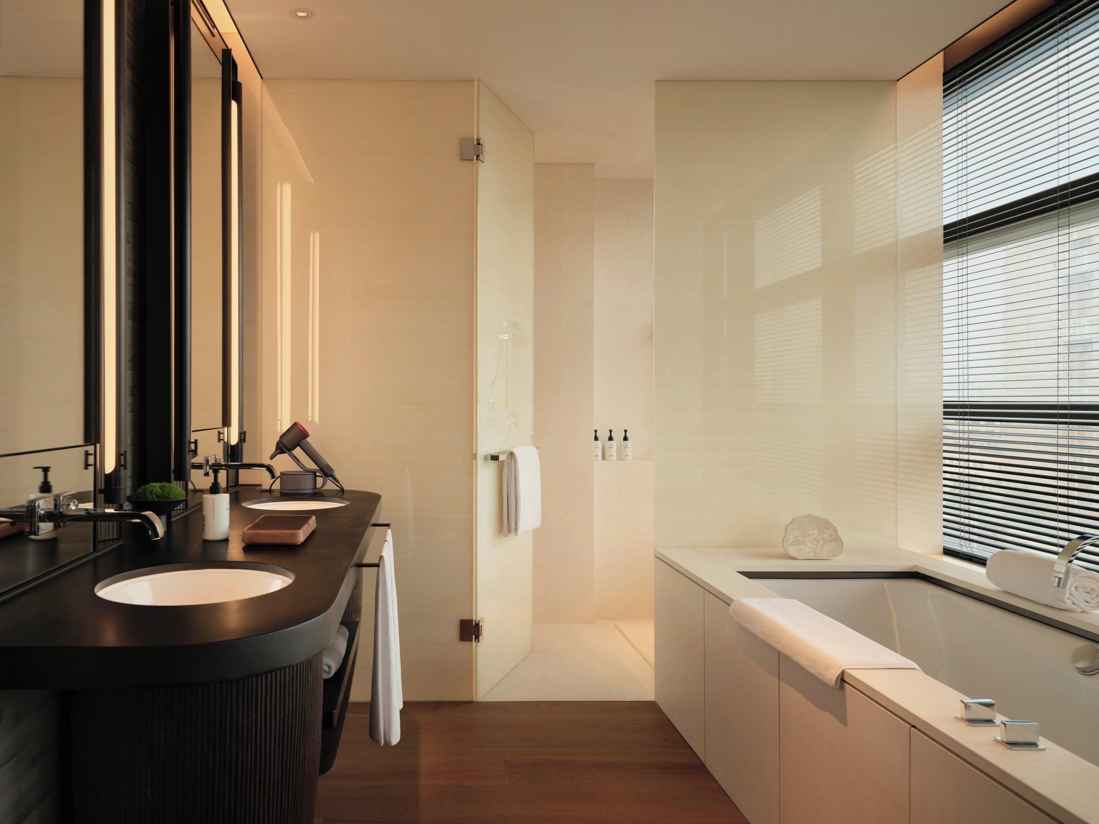 A modern bathroom with a double sink vanity, a large mirror, a towel rack, and a bathtub.
