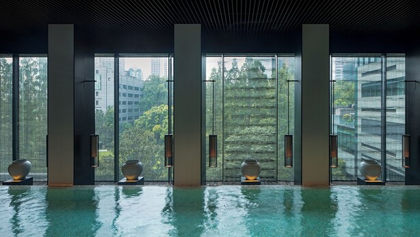 Un espace piscine intérieur moderne, doté de grandes fenêtres, de hauts piliers et de vases décoratifs.