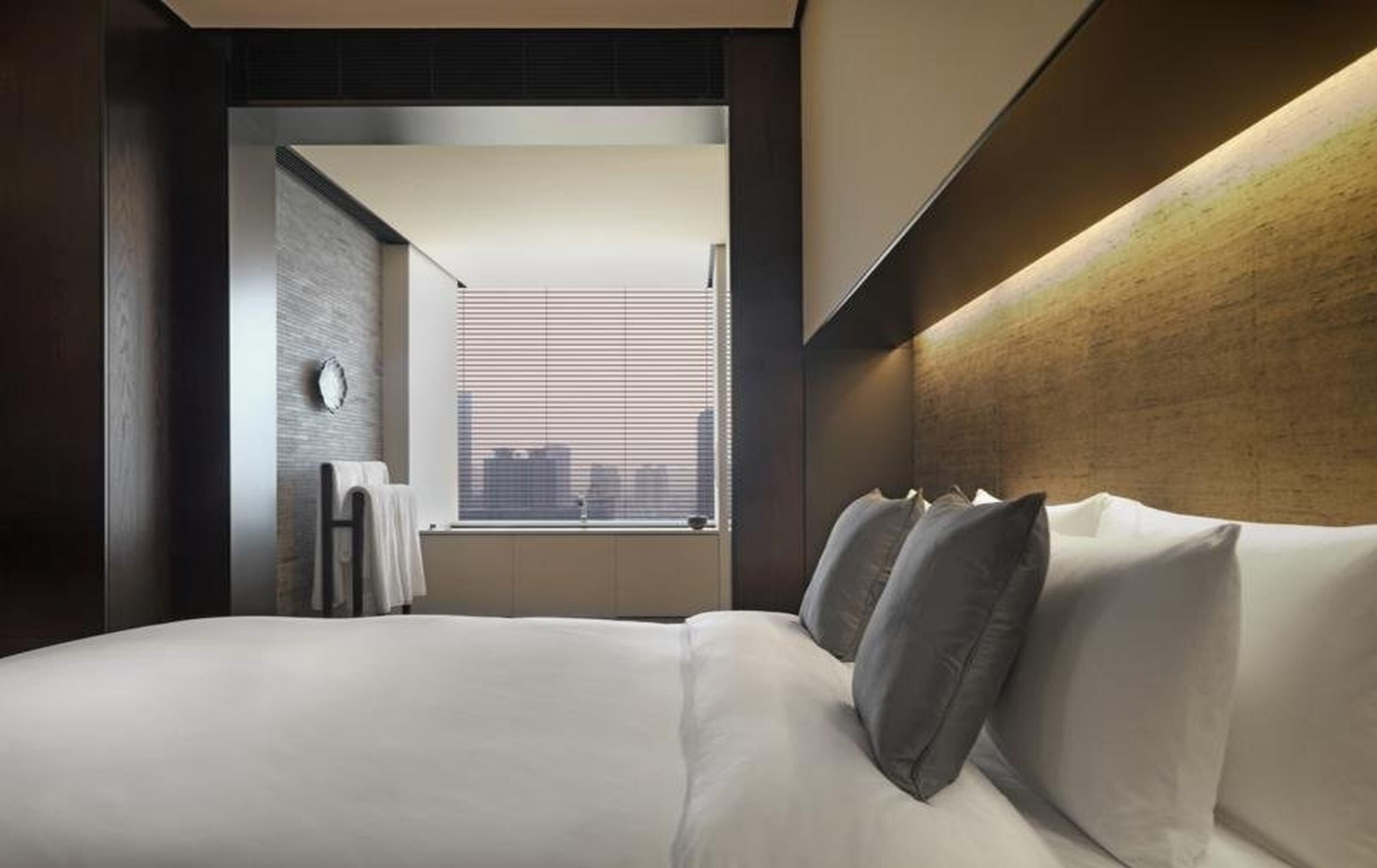 Una habitación de hotel moderna con una cama grande, vistas de la ciudad a través de la ventana y un cabecero de madera.