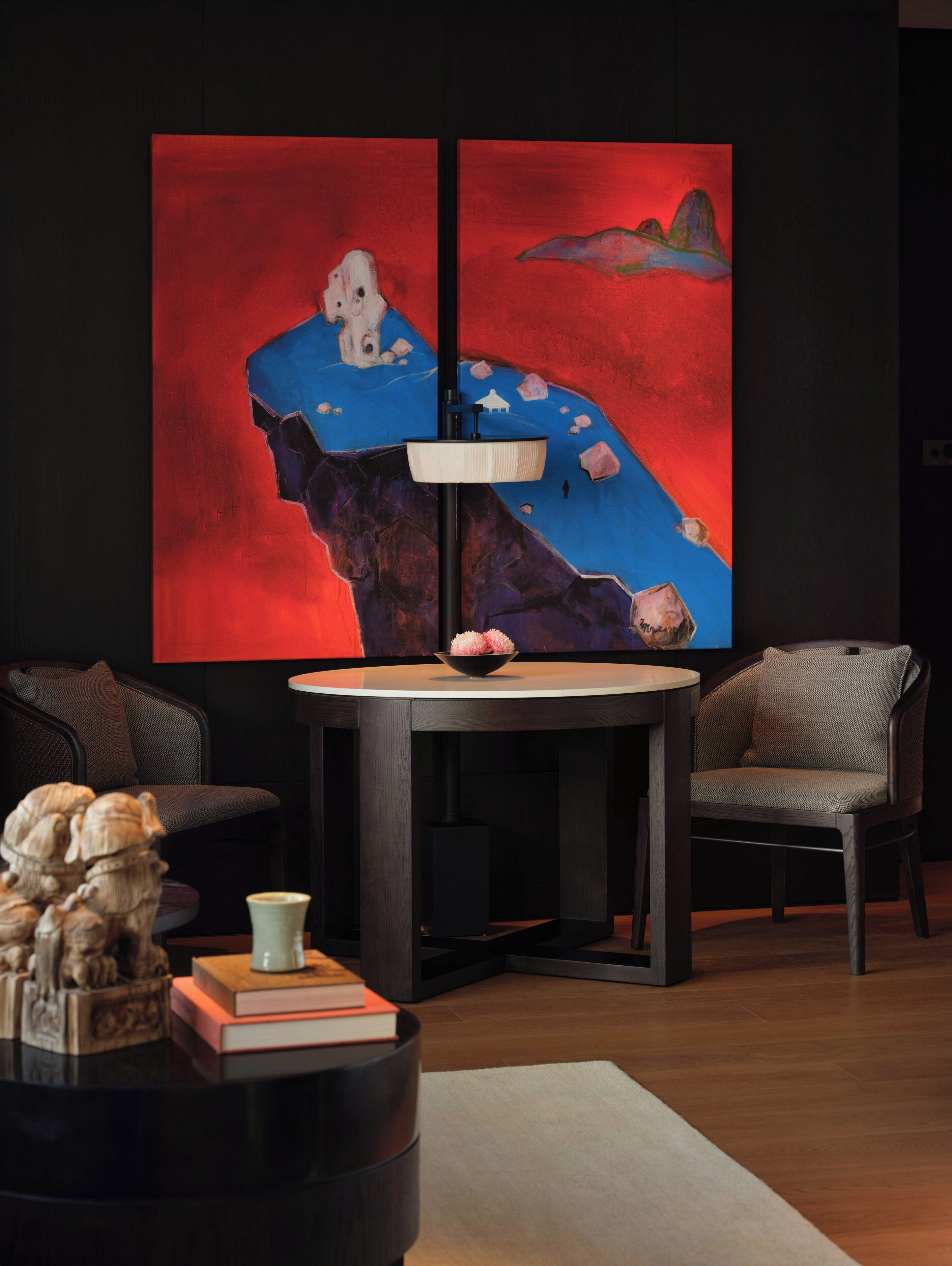 A modern living room with a round table, two chairs, a large abstract painting, and a sculpture on a side table.