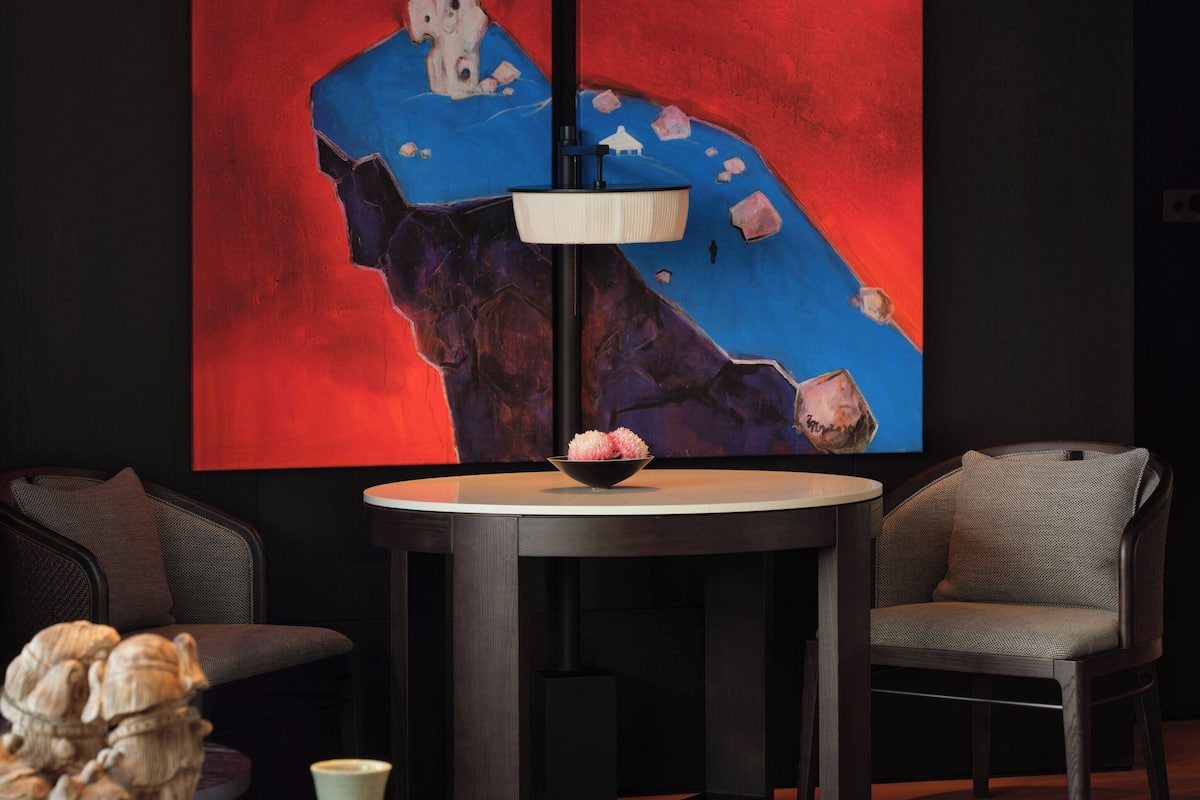 A modern living room with a round table, two chairs, a large abstract painting, and a sculpture on a side table.