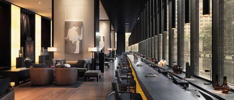 Un moderno vestíbulo de hotel con un mostrador de recepción alargado, zona de estar y grandes ventanales con vistas al exterior.
