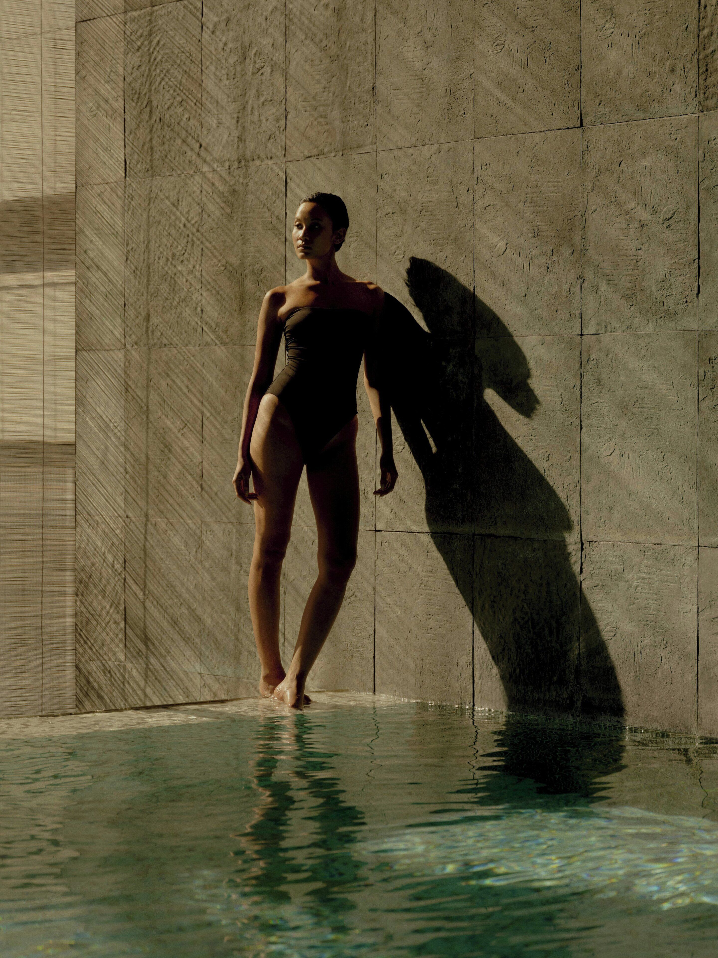 Una persona de pie en una piscina, con su sombra proyectada sobre una pared texturizada.