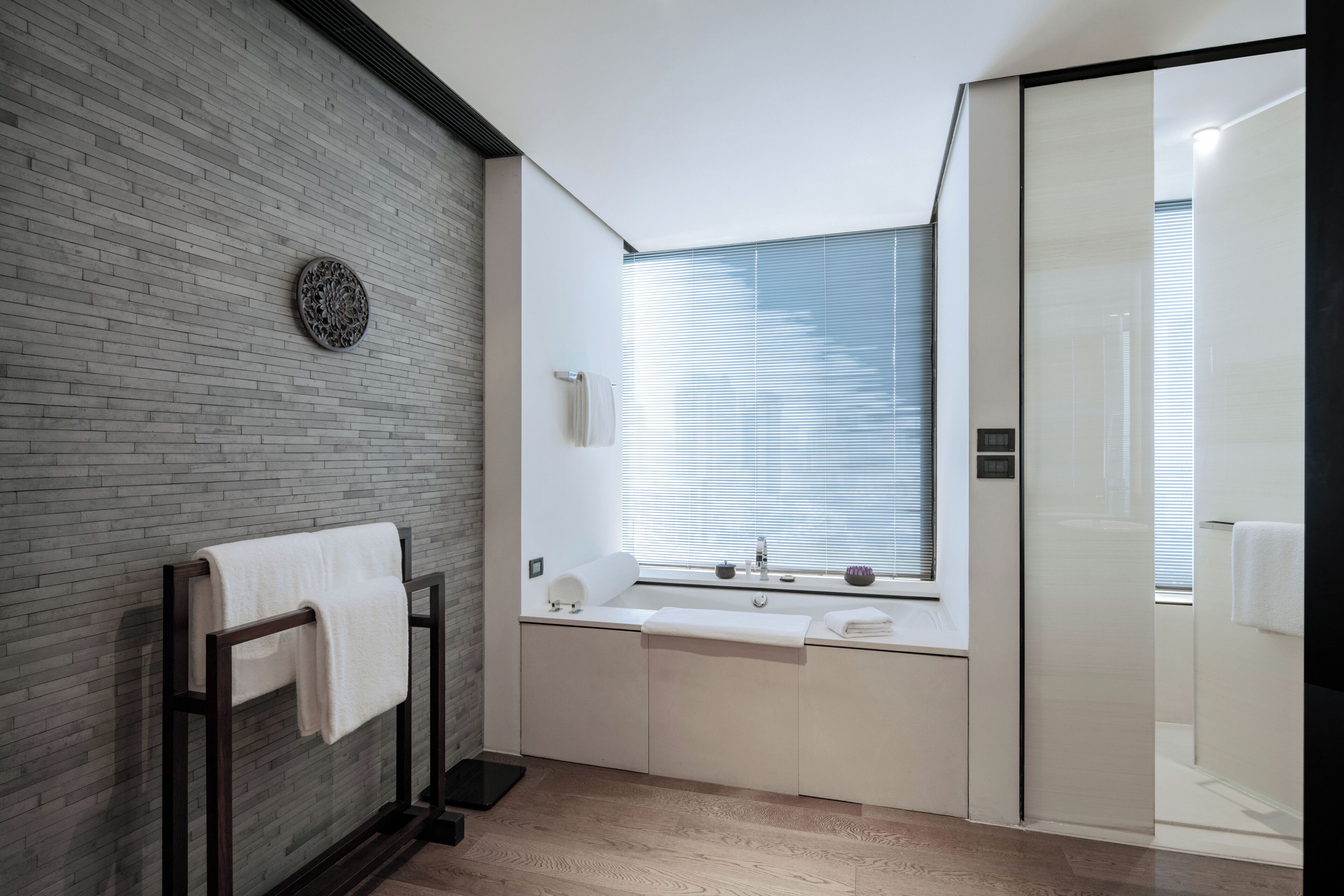 A modern bathroom with a brick wall, a towel rack, a sink with a mirror, and a shower area.