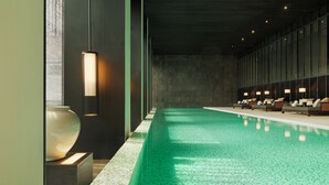Une piscine intérieure moderne, de forme longue et étroite, entourée d’espaces de détente avec des sièges et un éclairage d’ambiance.