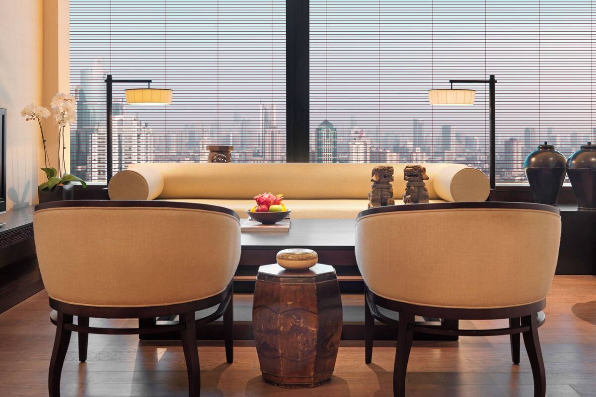 A modern living room with a sofa, two armchairs, a coffee table, and a view of a city skyline through large windows.