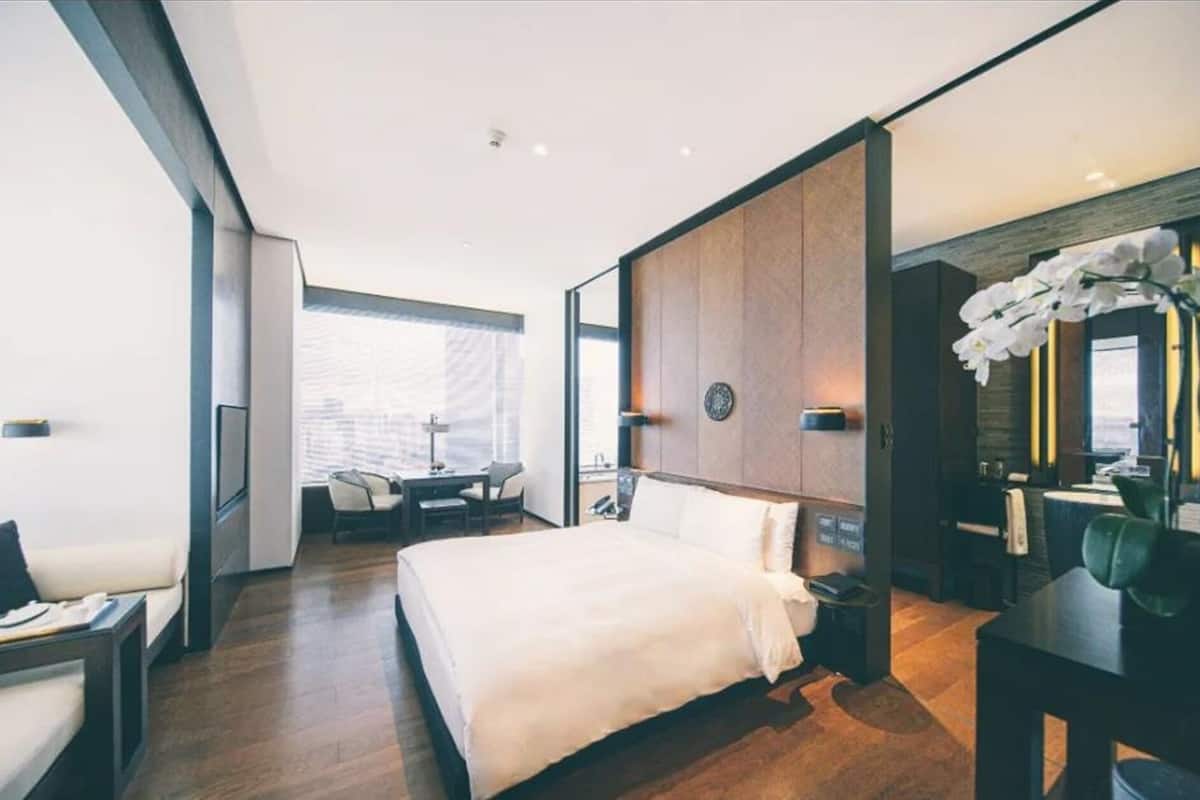 A modern hotel room with a large bed, a desk, and a seating area with chairs.