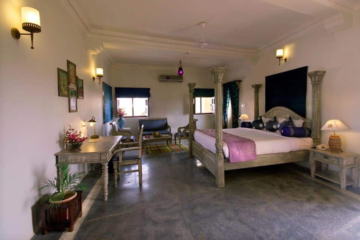 Ein Schlafzimmer mit einem Himmelbett, einem Schreibtisch mit Stuhl, einer Couch und einem kleinen Tisch mit Lampe.