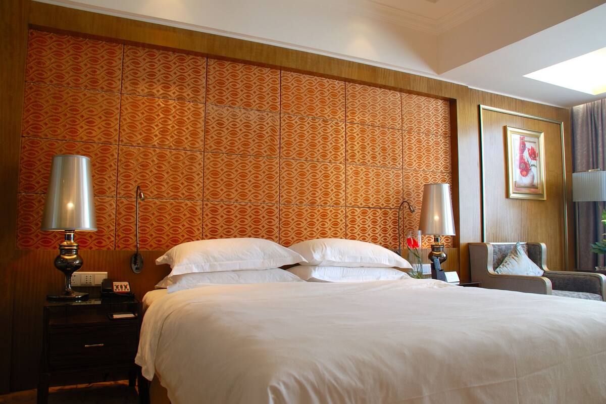 A hotel room with a large bed, two bedside lamps, a nightstand, and a chair.