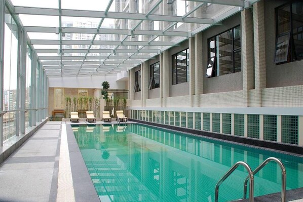 An indoor swimming pool with clear glass walls, a tiled floor, and a few lounge chairs. - Good International Hotel (Guangzhou)