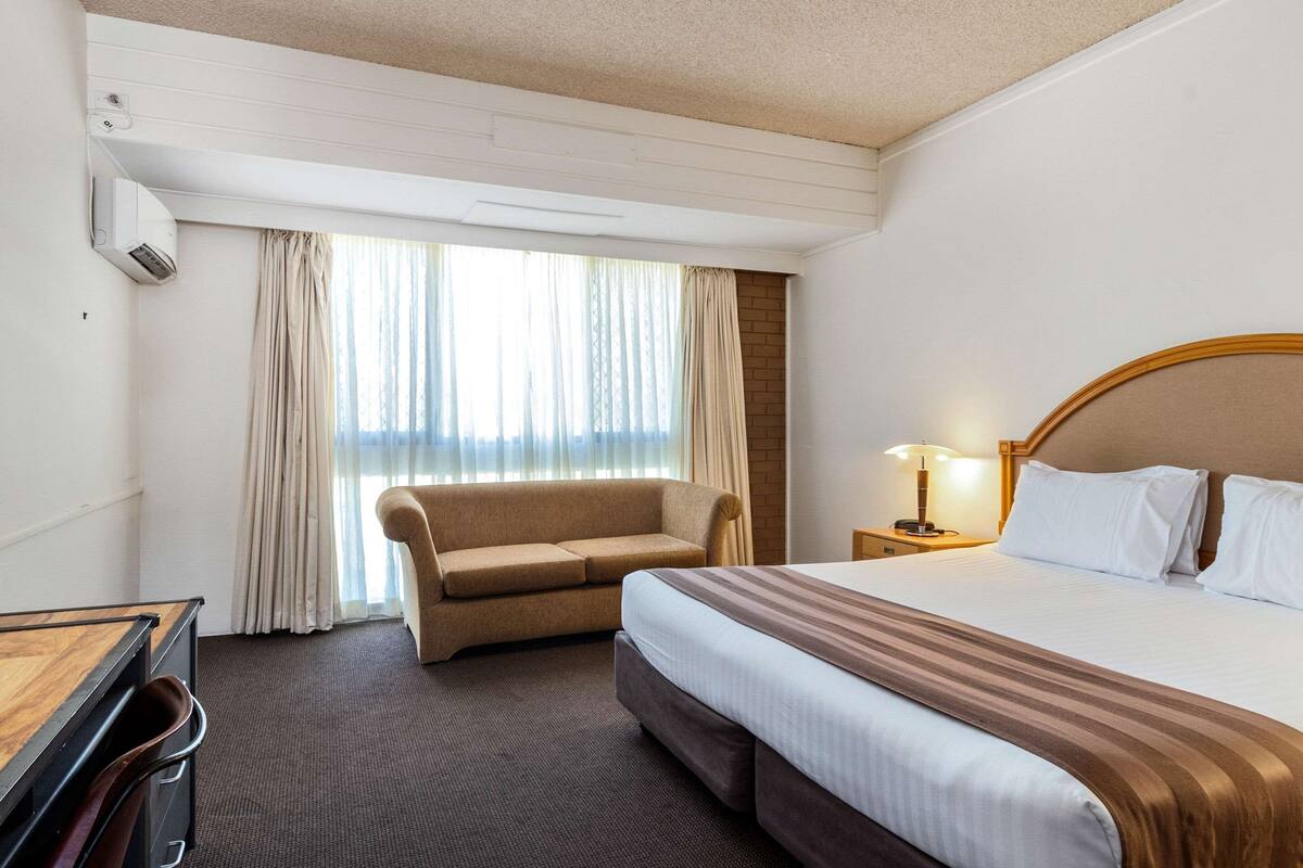 Una camera d'albergo con un letto, un divano, una scrivania e una finestra con tende.