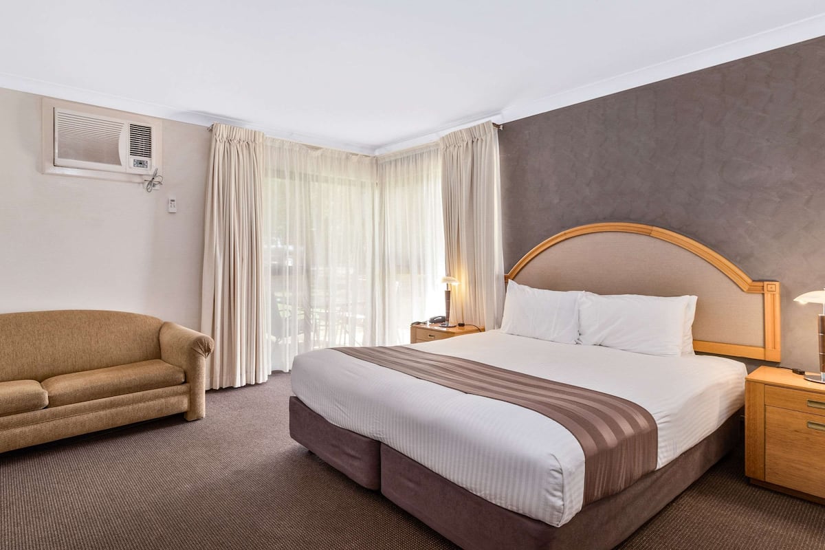 Una camera d'albergo con un letto grande, un divano, un comodino e una finestra con tende.