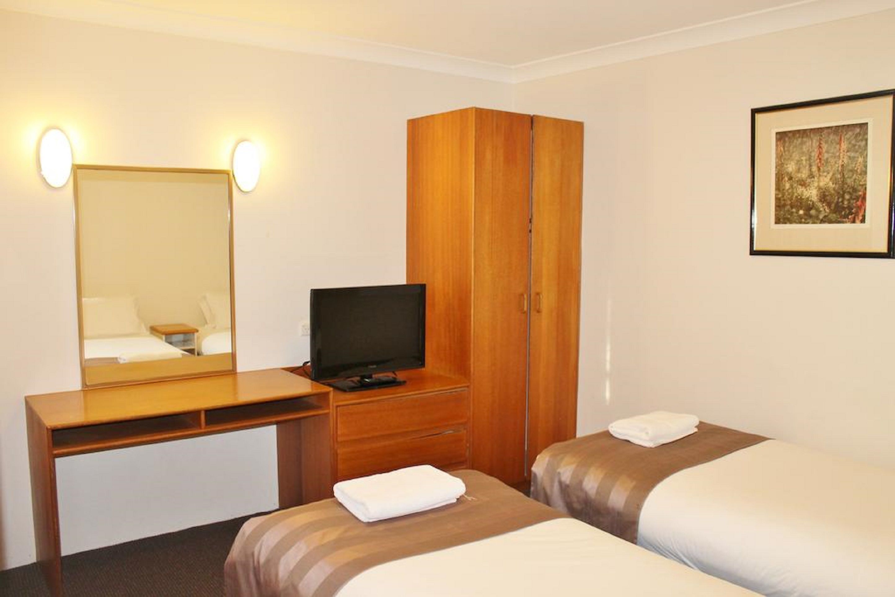 Habitación de hotel con un escritorio de madera, televisión, dos camas y un cuadro en la pared.