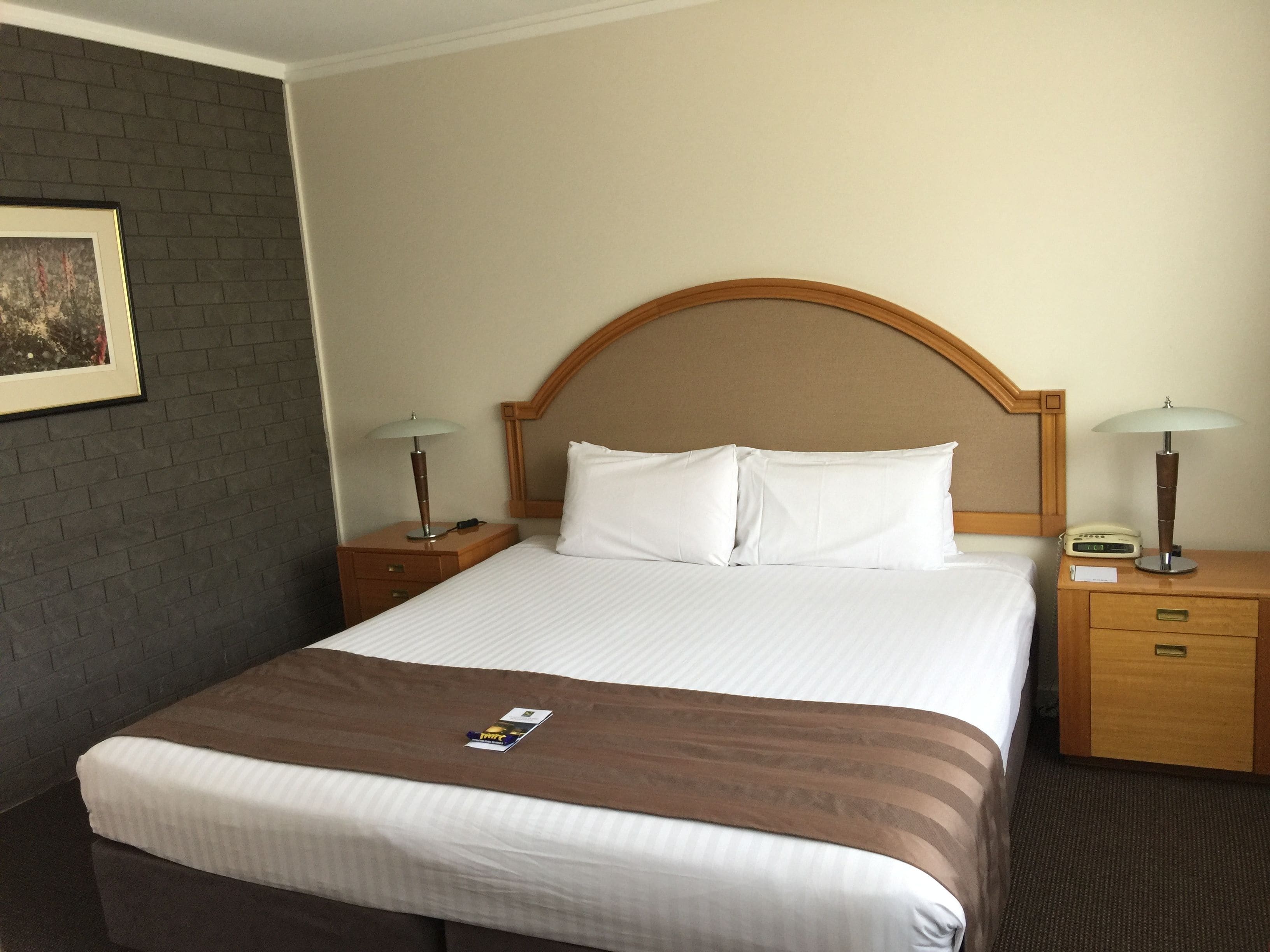 A hotel room with a large bed, two bedside tables, a wooden headboard, and a framed picture on the wall.