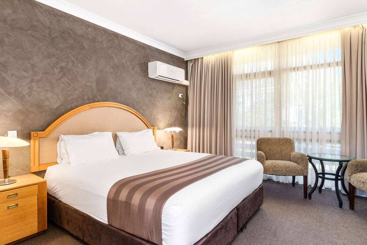 Una camera d'albergo con un letto grande, un comodino, una sedia, un tavolino e una finestra con tende.