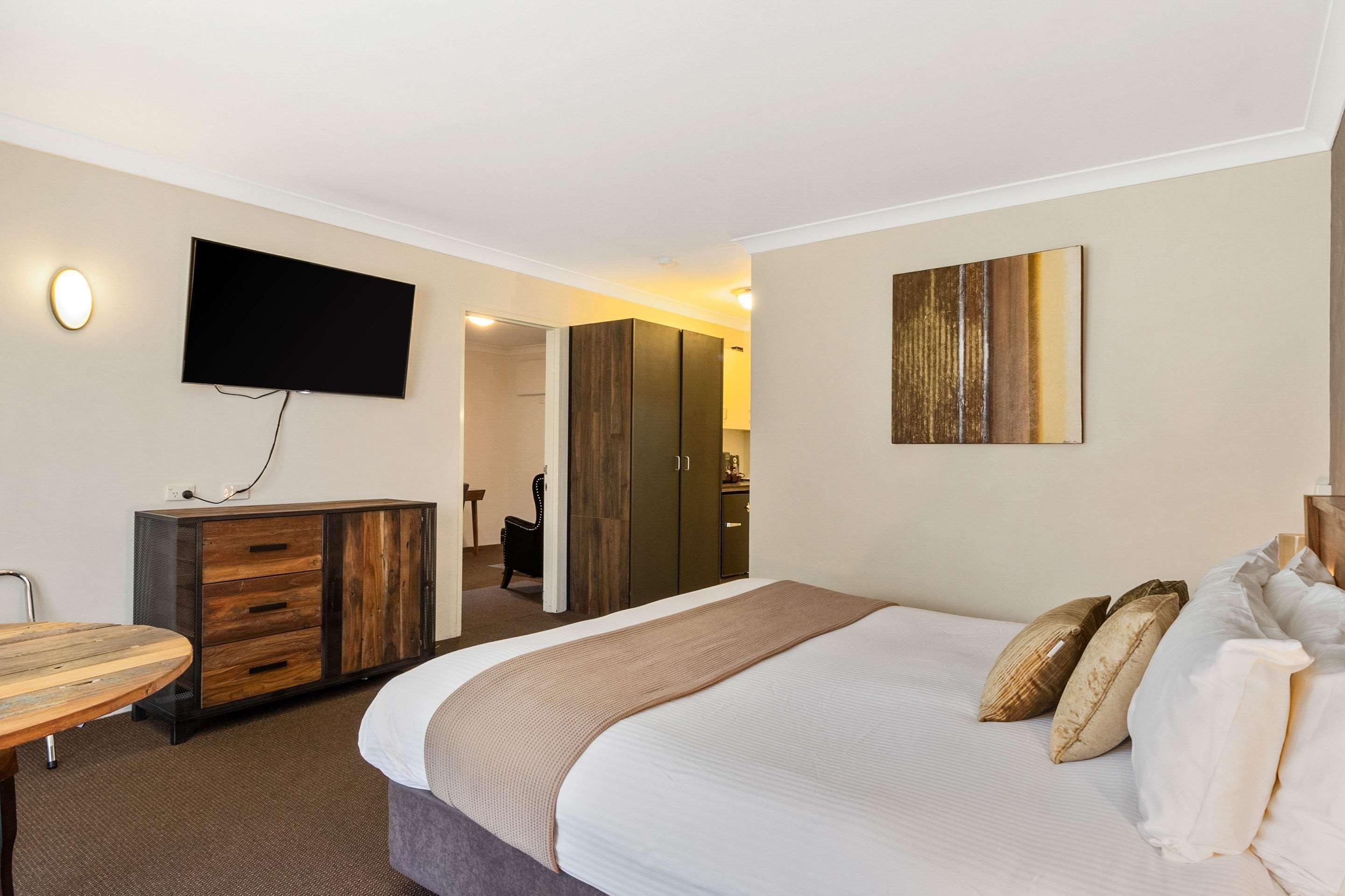 A hotel room with a bed, a TV mounted on the wall, a wooden cabinet, and a painting on the wall.