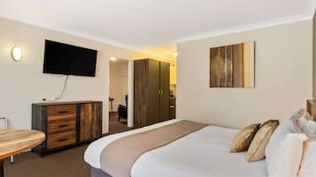 A hotel room with a bed, a TV mounted on the wall, a wooden cabinet, and a painting on the wall.