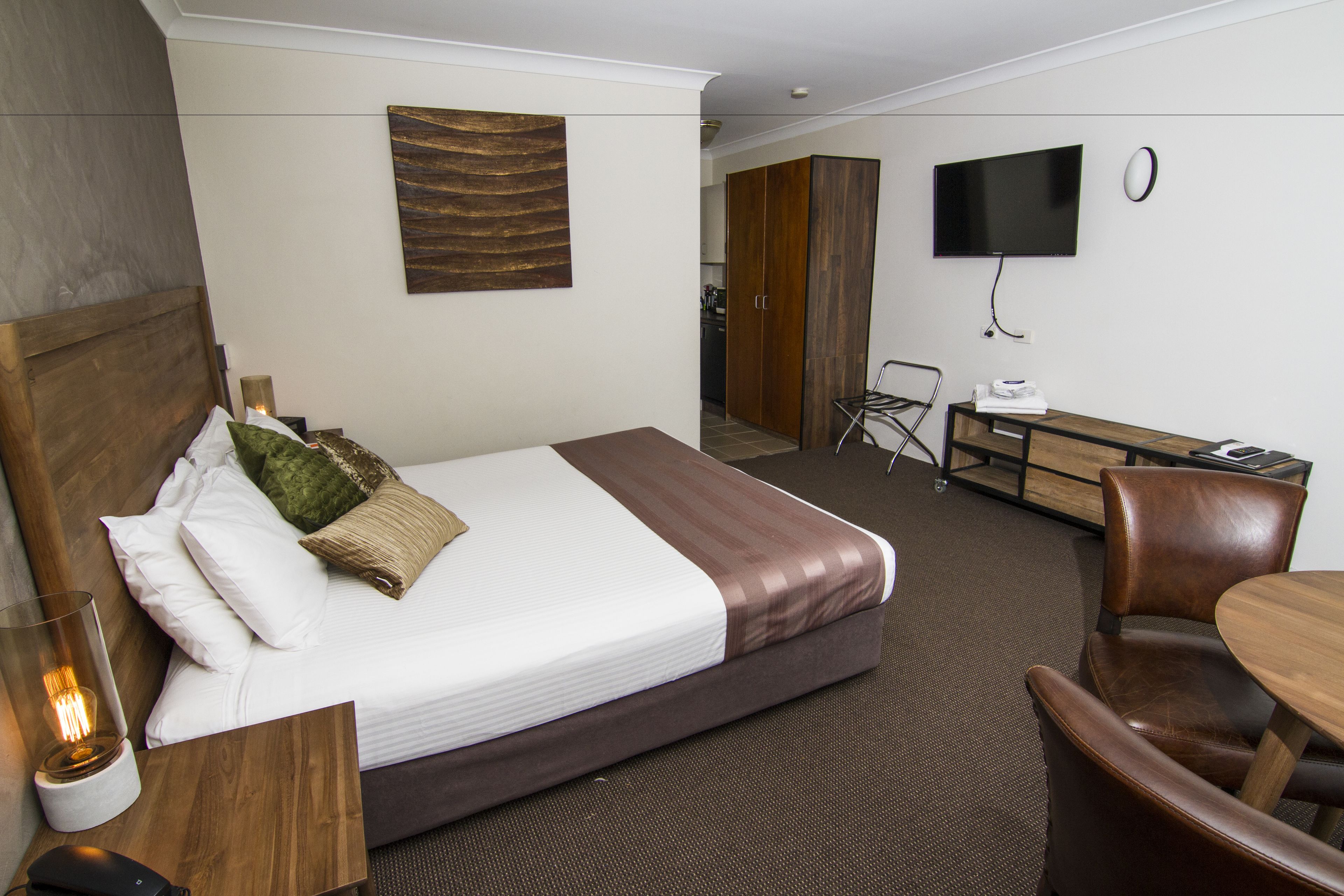 Ein Hotelzimmer mit einem Bett, einem Schreibtisch, einem Sessel, einem Fernseher und einem Wandbild.