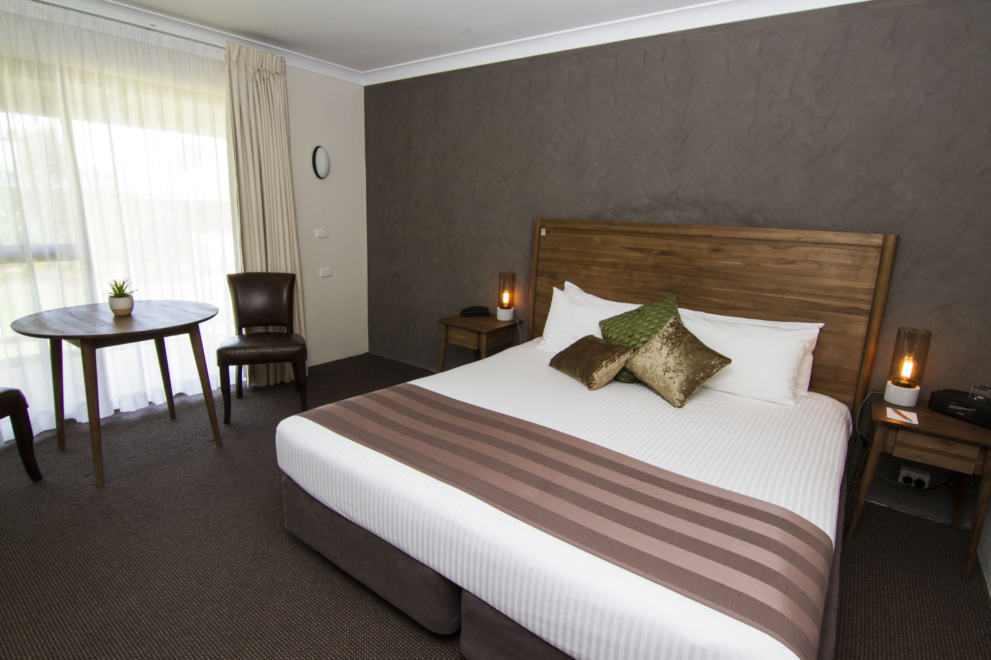 Habitación de hotel con una cama grande, una mesa redonda con una silla y una mesita con una planta.