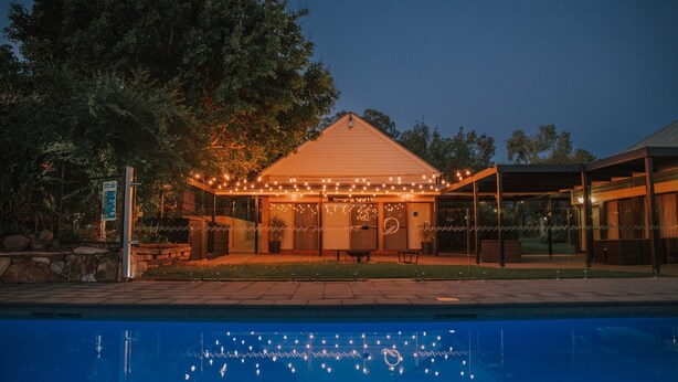 Zona de piscina con un área de descanso cubierta, un cartel y un edificio con luces colgantes.