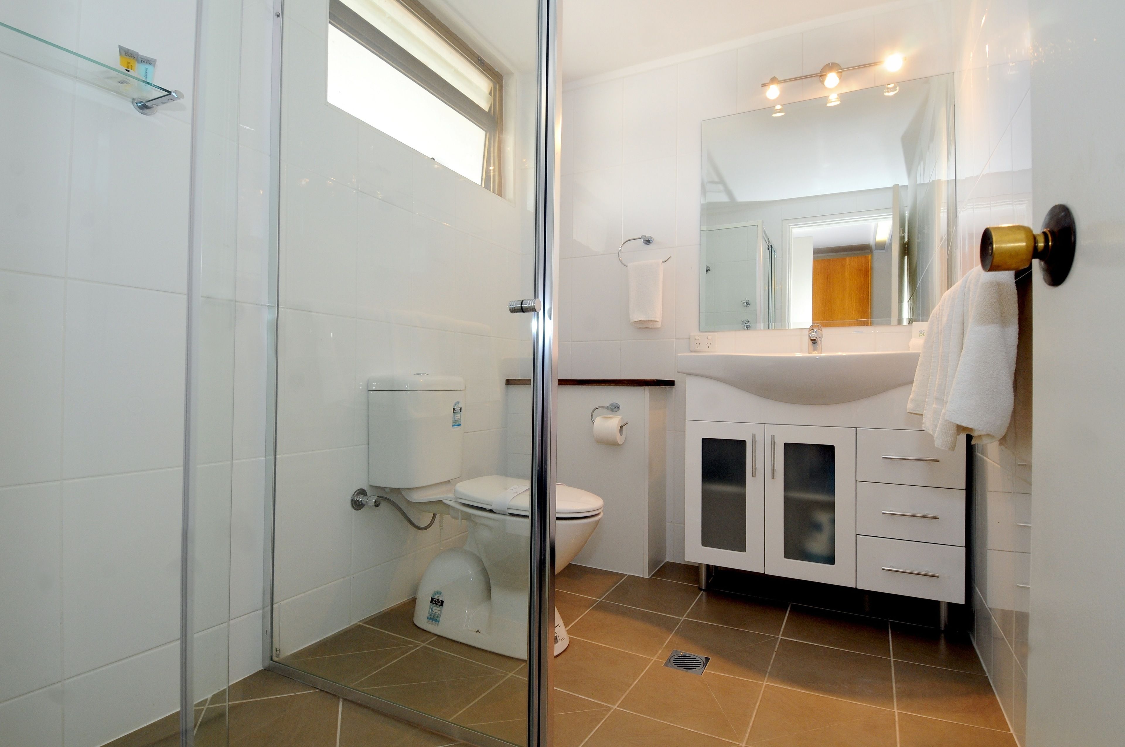 A modern bathroom with a glass shower enclosure, a white toilet, a sink with a mirror, and a towel rack.