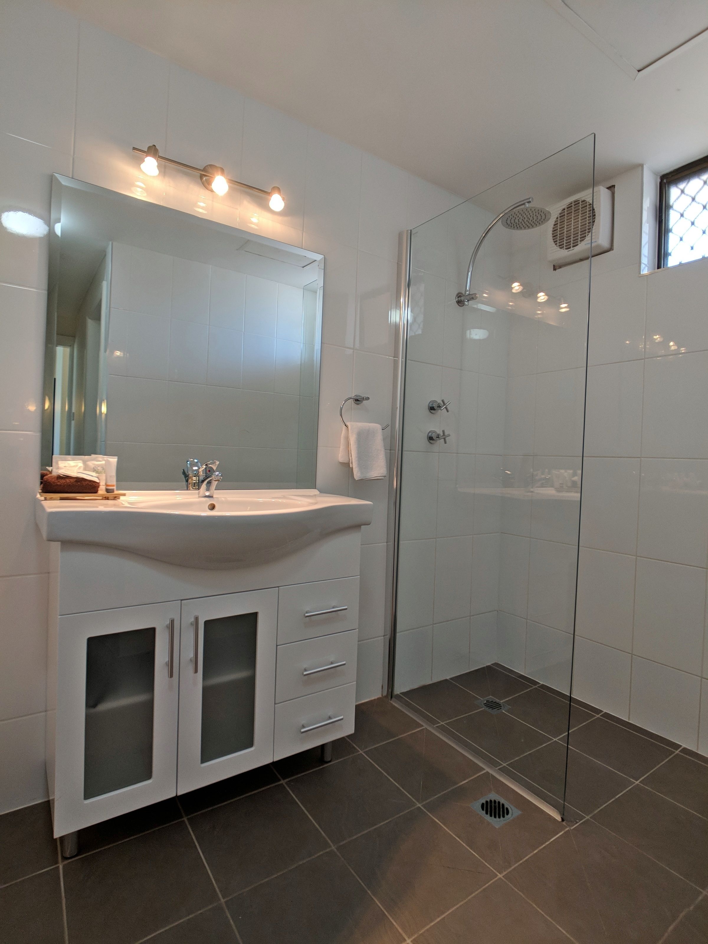 A modern bathroom with a white sink, mirror, and glass shower enclosure.