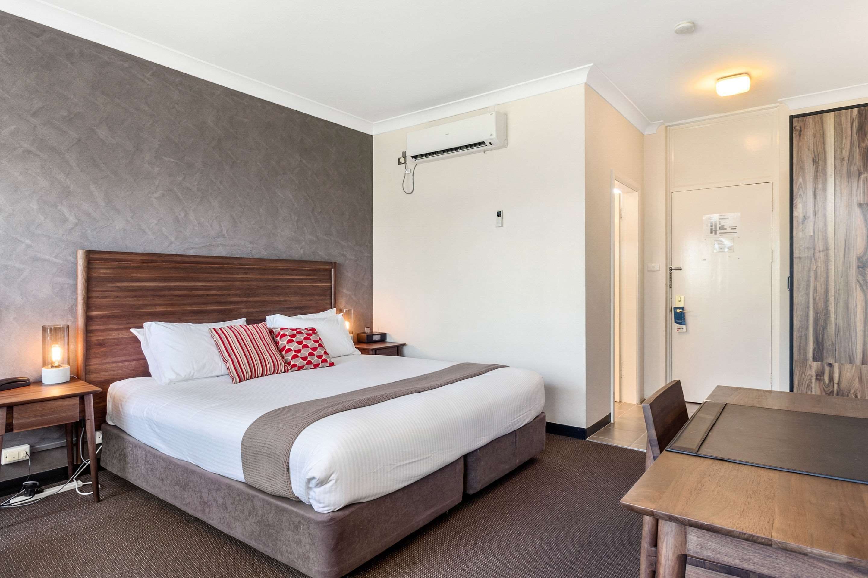 A hotel room with a large bed, bedside tables, an air conditioning unit, a wooden door, and a dining table.