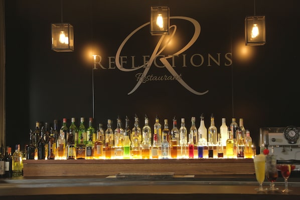 A bar with a variety of liquor bottles and glasses, illuminated by hanging lights. - Quality Inn Dubbo International (Dubbo)