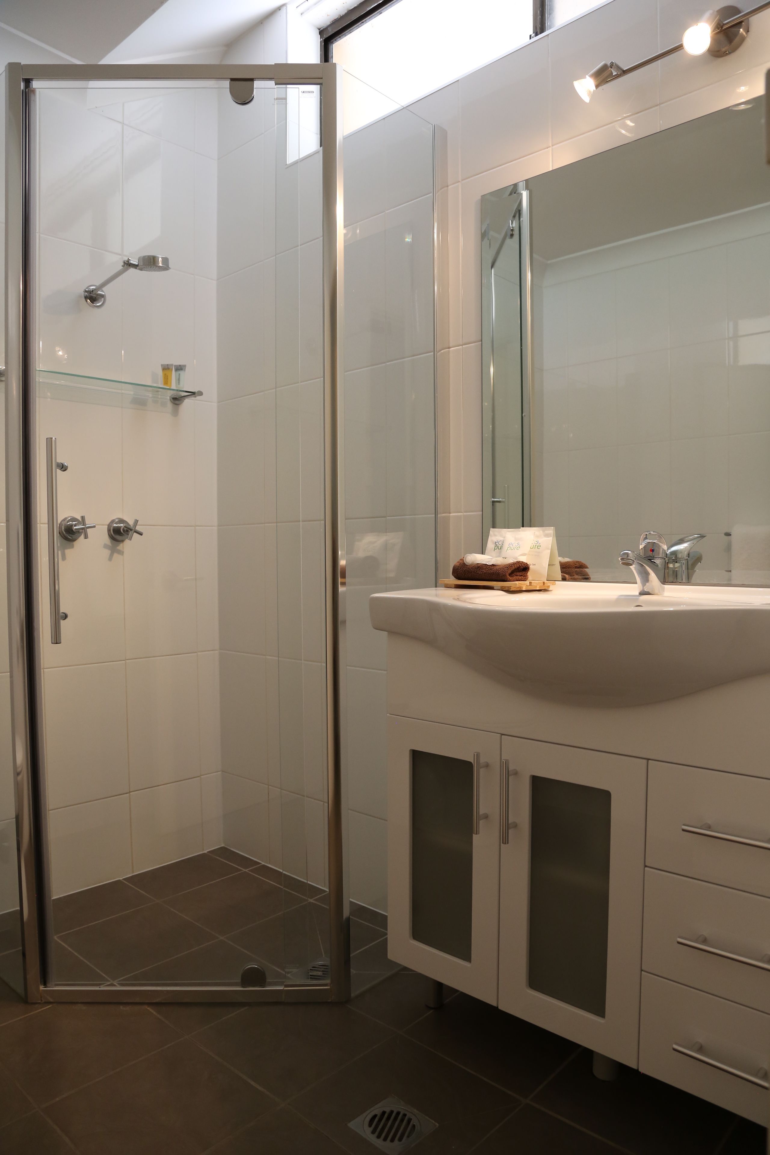 A modern bathroom with a glass-enclosed shower, a white sink with a mirror above it, and a cabinet with drawers.