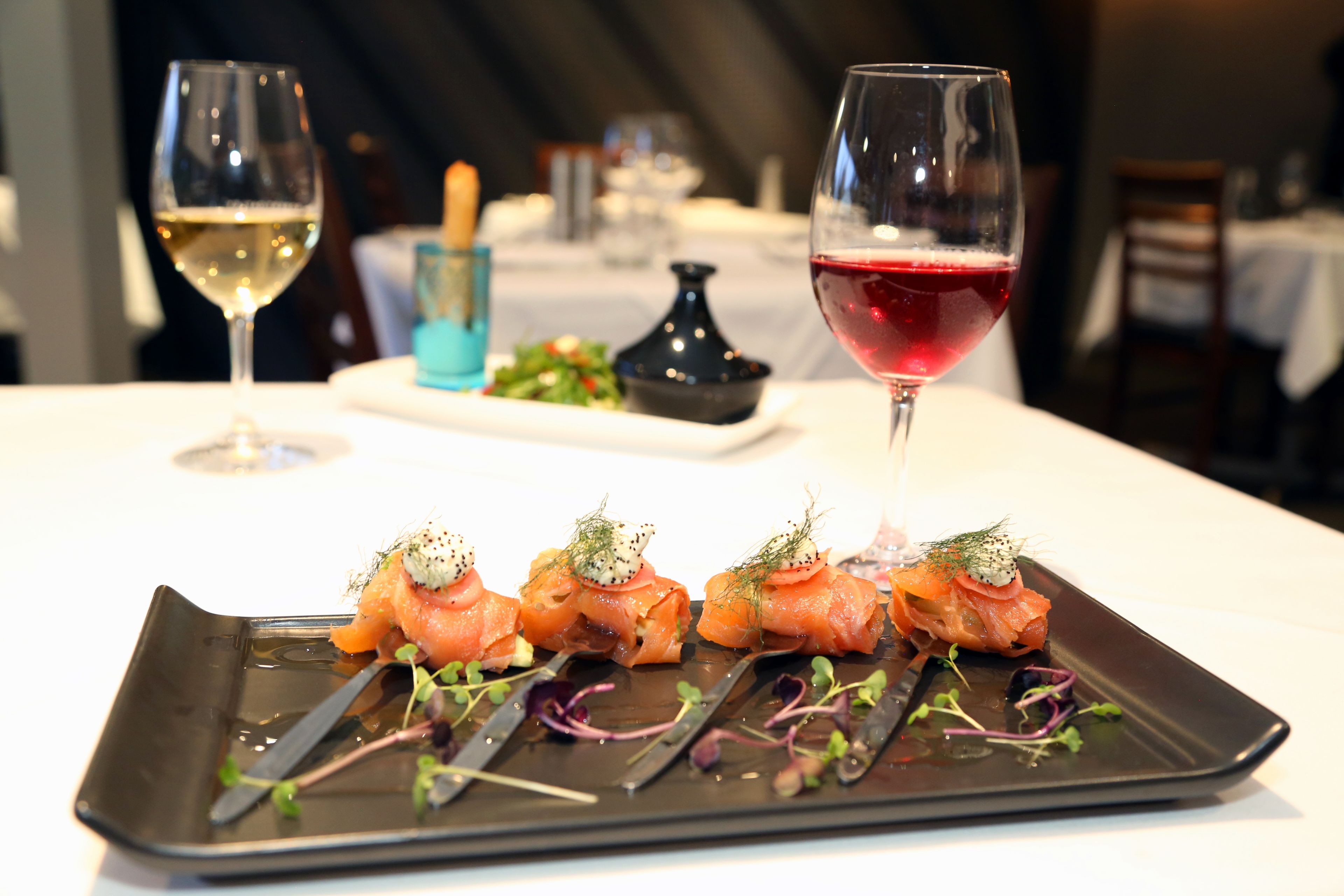 A dining table with a black plate of food, two glasses of wine, and a small blue dish in the background.