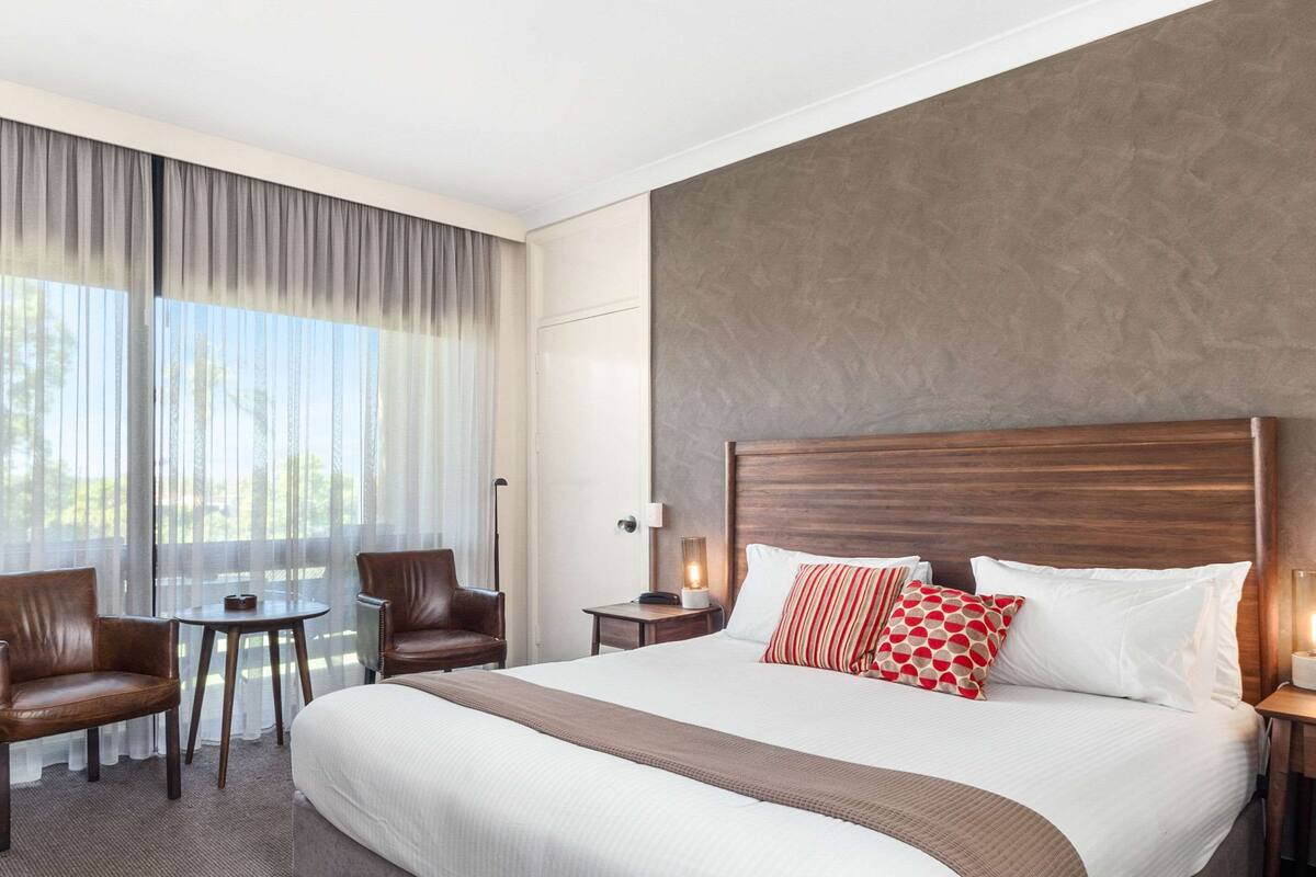Una camera d'albergo con un letto grande, due poltrone, un tavolino e un comodino con una lampada.