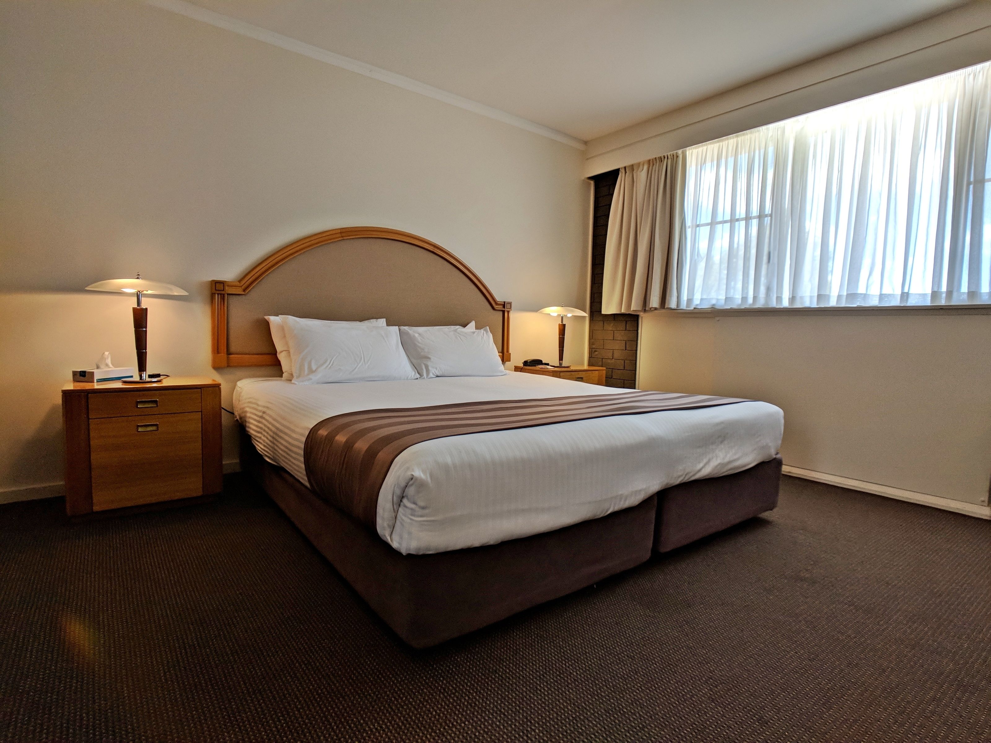 Une chambre d’hôtel avec un grand lit, deux tables de chevet, une petite table et une fenêtre avec des rideaux.