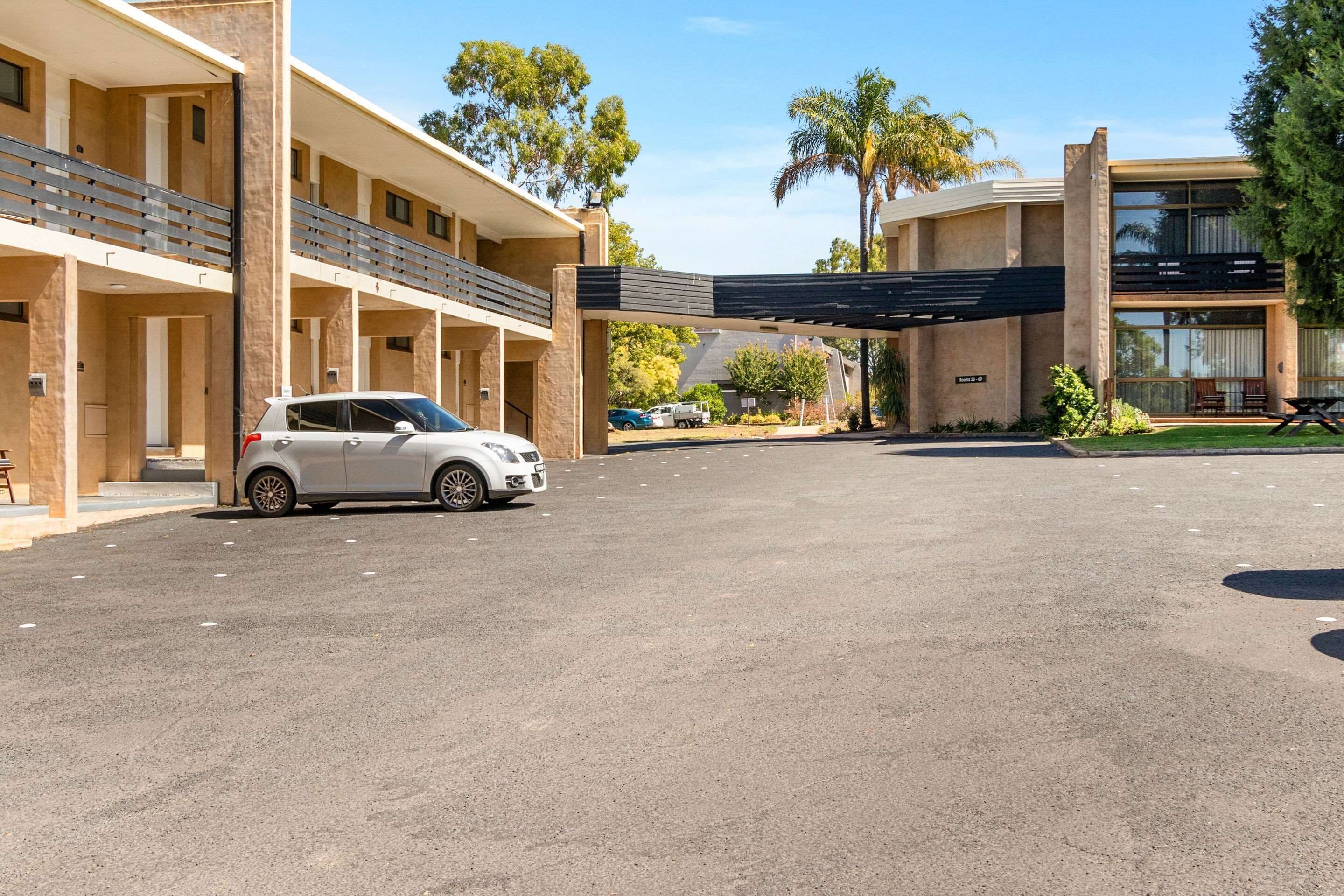 Un hotel de varios pisos con una zona de estacionamiento techada y un coche blanco estacionado al frente.