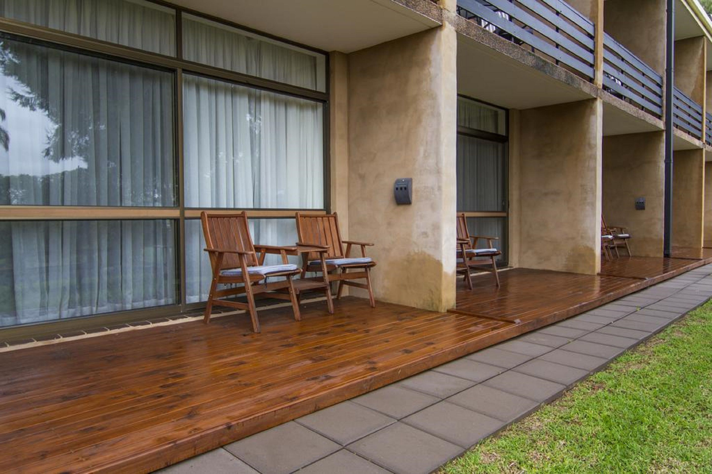 Un edificio moderno con un espacio exterior cubierto que incluye sillas de madera y piso de baldosas.