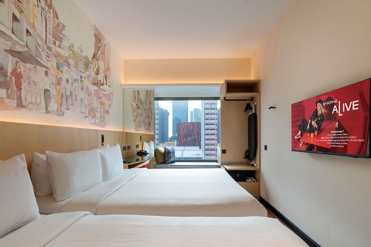 A hotel room with two beds, a large window, a wall-mounted TV, and a view of the city.