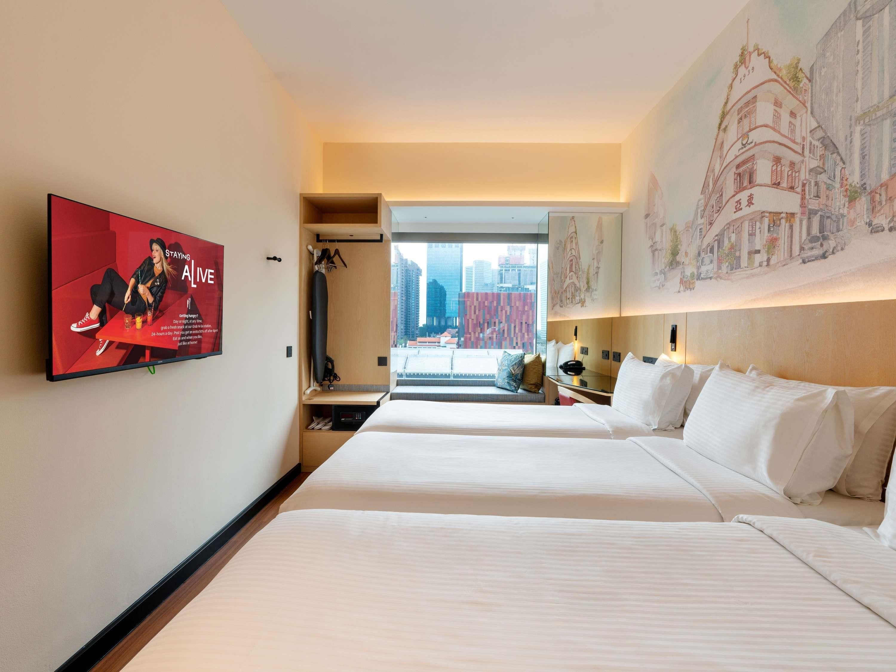 A hotel room with two beds, a TV, a desk, and a view of the city.