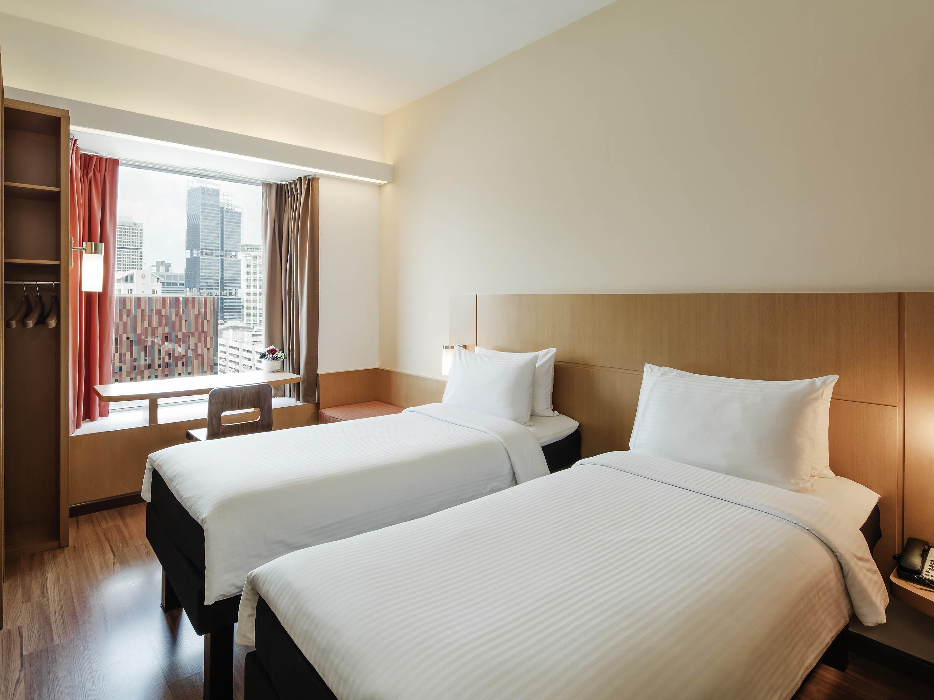 Habitación de hotel con dos camas, un escritorio y vistas a la ciudad.