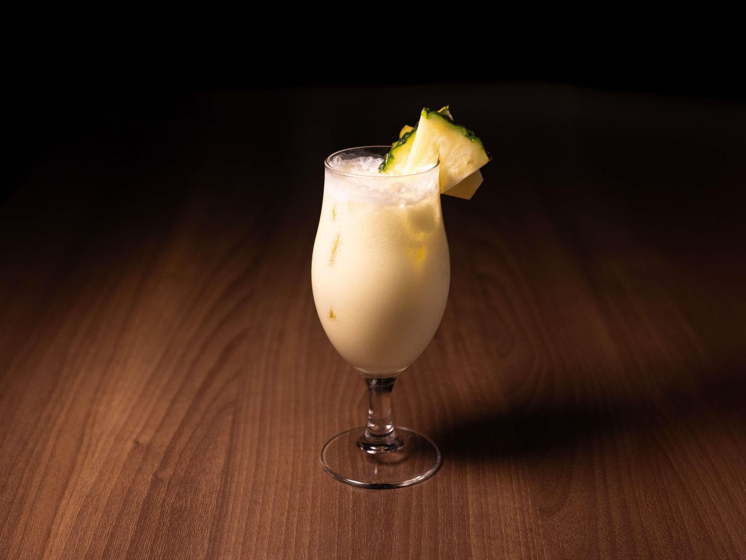 A glass of a creamy beverage with a pineapple garnish on a wooden surface.