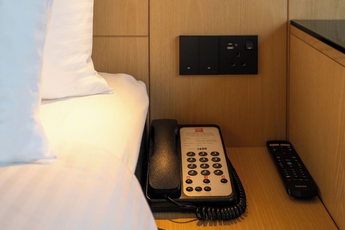 Et hotelværelse med en seng, en telefon og en fjernbetjening på et natbord i træ.