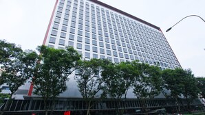 Un immeuble moderne et imposant, doté d’une façade à carreaux de fenêtres et d’une bande rouge en haut.