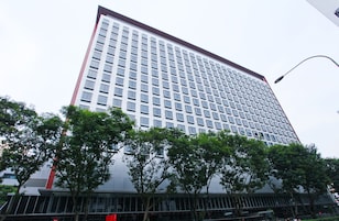 A tall, modern building with a grid of windows and a red trim at the top.