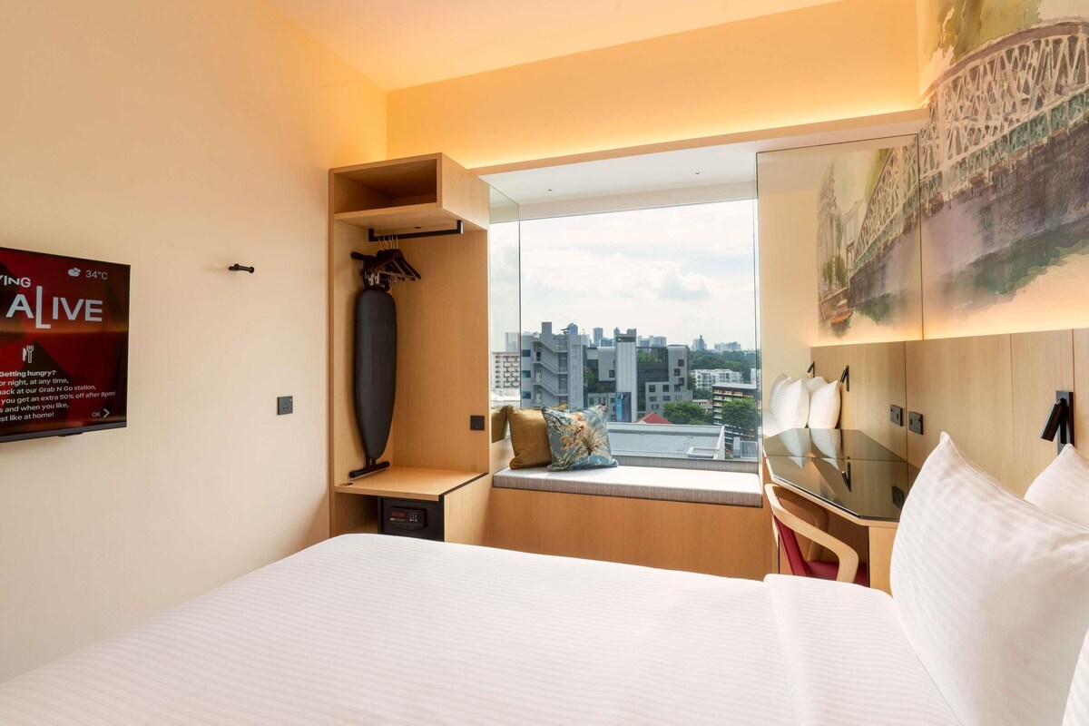 Hotelkamer met een groot bed, een raam met uitzicht op de stad, een klein bureau en een kapstok.