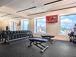 Un gimnasio con mancuernas, bancos y vistas a la ciudad.